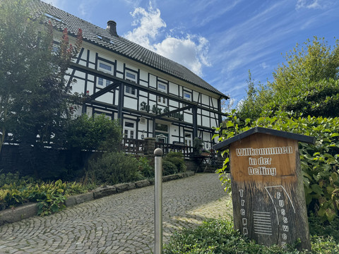 In der Delling Außenansicht Fachwerkhaus mit Steingarten und Schild am Eingang bei sonnigem Wetter und blauem Himmel.