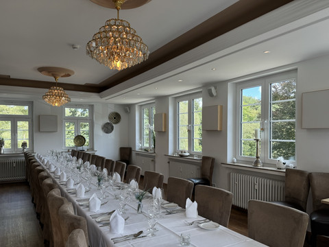 Innenansicht Eleganter, lichtdurchfluteter Speiseraum mit langen Tafeln, Kristallkronleuchtern und großen Fenstern.