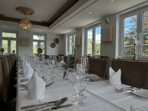 Innenansicht Elegantes Speisezimmer mit langem, festlich gedecktem Tisch, Kerzenleuchtern und Blick auf grüne Bäume.