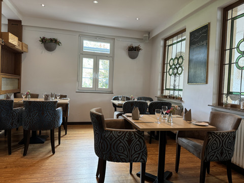 Innenansicht Gemütliches Café-Interieur mit Holztischen, gepolsterten Stühlen und Fenstern mit floralen Mustern.