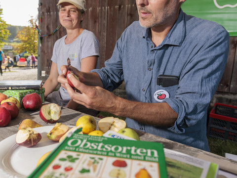 Obstwiesenfest Ein Mann und eine Frau präsentieren verschiedene Obstsorten an einem Marktstand unter einem Pavillon.