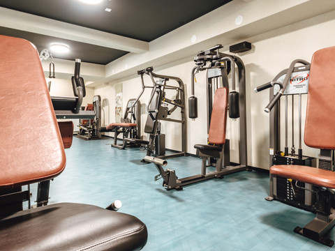 Fitnesspark (10).jpg Moderner Fitnessraum mit mehreren Kraftgeräten, ausgestattet mit roten Ledersitzen und blauem Boden.