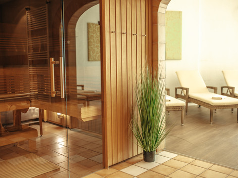 Wellness (2).jpg Holzverkleidete Sauna mit Glasfront, Pflanzen und Liegestühlen auf hellem Boden in einem Entspannungsraum.