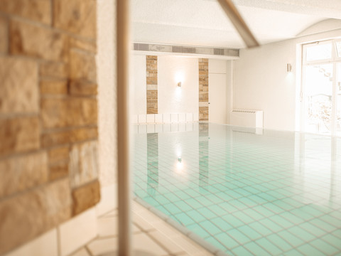 Wellness (4).jpg Beheiztes Hallenbad mit hellblauen Fliesen, natürlichem Licht und gemauerten Akzenten in einem Wellnessbereich.