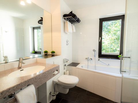 Badezimmer (2).jpg Helles Bad mit großer Badewanne, modernem Waschbecken, Fenster, Toilette und kleinen grünen Pflanzen.