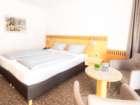 Zimmer (3).jpg Helles, modernes Hotelzimmer mit Doppelbett, zwei Sesseln und Tisch, stilvoll dekoriert.
