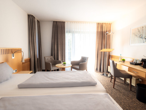 Zimmer (4).jpg Helles, modern eingerichtetes Hotelzimmer mit Doppelbett, Schreibbereich und Sitzgruppe.
