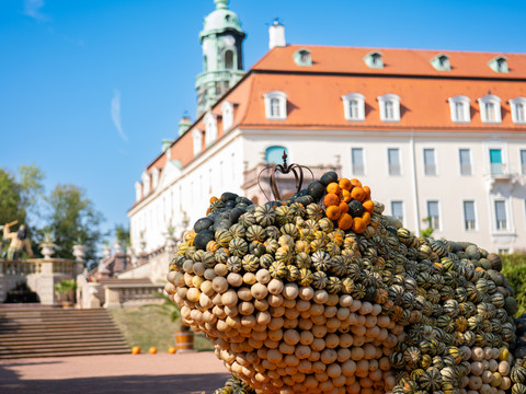 Large frog sculpture made of pumpkins in front of Lichtenwald Castle, blue sky in the background.