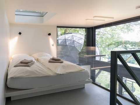 Innenansicht Baumhaus Modernes Schlafzimmer in einem Glashaus mit Blick auf Bäume und Gewölbekuppel, minimalistisch gestaltet.