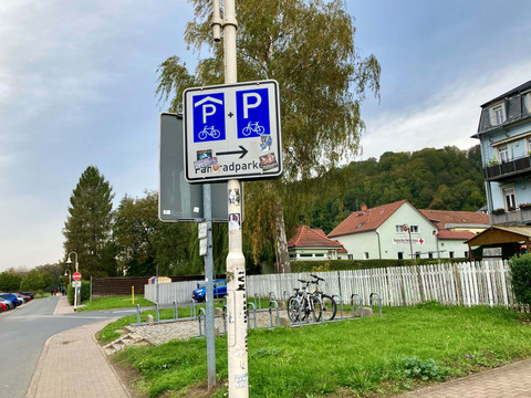 Bord fietsgarage Ein Straßenschild weist auf einen Fahrradparkplatz hin, im Hintergrund sind ein Gebäude des Deutschen Roten Kreuzes und eine grüne Landschaft zu sehen.