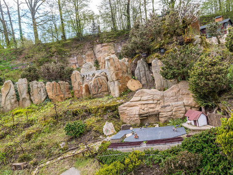 Miniaturpark "Kleine Sächsische Schweiz" Miniaturmodell einer Landschaft mit Felsen, kleinen Gebäuden und Vegetation, umgeben von Bäumen unter einem bewölkten Himmel.