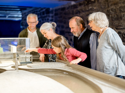 Wasserkraft im Aggertal Fünf Personen, darunter ein Kind, betrachten gemeinsam ein Wassermodell in einem Museumsraum.
