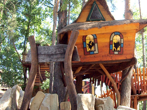 Kinderbaumhaus Erhöhtes Baumhaus mit buntem Fensterglas, eingebettet in einen Waldspielplatz.Raised tree house with colorful window glass, embedded in a forest playground.Vyvýšený domek na stromě s barevnými okenními skly, zasazený do lesního hřiště.Podniesiony domek na drzewie z kolorowymi szybami, osadzony w leśnym placu zabaw.Verhoogde boomhut met kleurrijk vensterglas, ingebed in een bosspeeltuin.Casa sull'albero rialzata con vetri colorati, inserita in un parco giochi nella foresta.