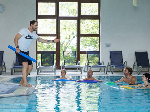Trans World Hotel Kranichhöhe Ein Trainer im weißen Shirt leitet eine Aqua-Fitnessstunde an, während vier Personen im Pool trainieren.