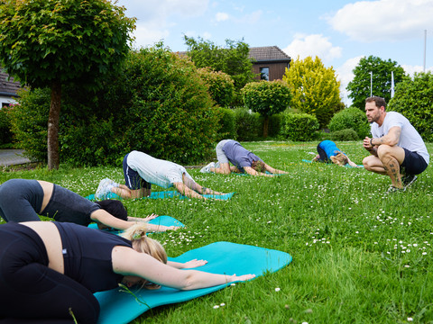 Trans World Hotel Kranichhöhe Menschen in einer Yoga-Gruppe praktizieren im Freien auf einer grünen Wiese verschiedene Entspannungspositionen.