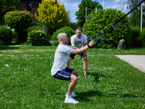 Trans World Hotel Kranichhöhe Zwei Männer trainieren im Freien mit einem Spannungsseil auf einer grünen Rasenfläche.