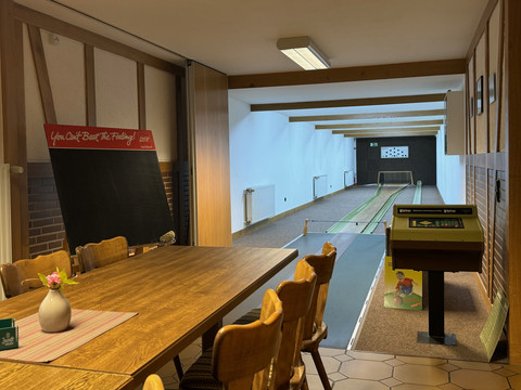 Landhaus Fuchs - Kegelbahn Gemütlicher Kegelraum mit Holztisch, Kegelbahn im Hintergrund, rustikale Atmosphäre.