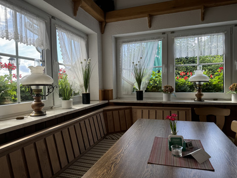 Landhaus Fuchs - Ansicht Innenbereich Gemütliche Fensterbank mit Holztisch, dekoriert mit Blumen und rustikalen Lampen vor großen Fenstern.