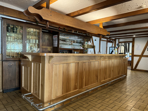 Landhaus Fuchs - Ansicht Bar Holztresen in rustikaler Gaststube mit Holzbalken, Gläsern und Flaschen im Hintergrund.