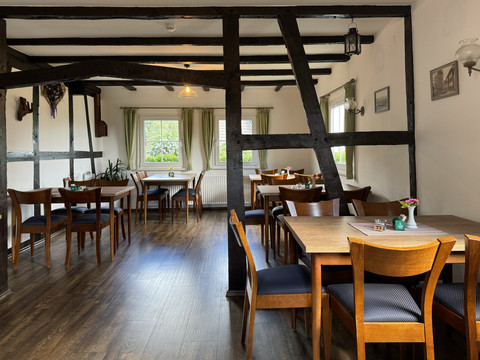 Landhaus Fuchs - Ansicht Innenbereich Gemütlicher Gastraum mit Holzbalken, gedeckten Tischen, Stühlen und Blick nach draußen durch Fenster.