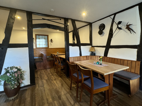 Landhaus Fuchs - Ansicht Innenbereich Gemütlicher Gastraum in Fachwerkstil mit Holzmöbeln und Dekorationen, warme Beleuchtung über Tischen.
