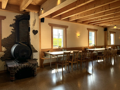 Jägerhof - Veranstaltungsraum Gemütlicher Gastraum mit langen Holztischen, Stühlen und einem Kaminofen an der Backsteinwand.