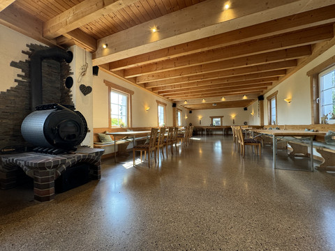 Jägerhof - Veranstaltungsraum Großer, rustikaler Gastraum mit Holzbalkendecke, Holzvertäfelung, langen Tischen und einem Kaminofen.