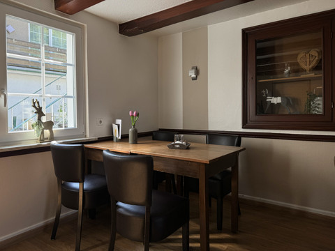Jägerhof - Innenbereich Gemütliches Esszimmer mit Holztisch, vier schwarzen Stühlen und Fenstern, viel natürliches Licht.