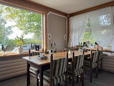 IMG_2928.jpeg Essbereich mit Holztisch und gepolsterten Stühlen, große Fensterfront mit Blick ins Grüne und Dekoration.