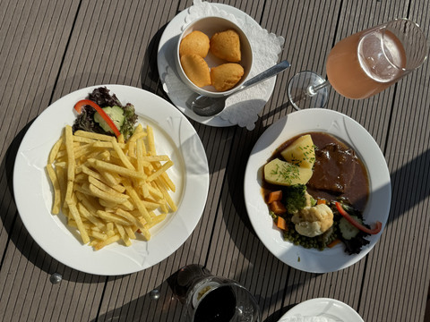 Jägerhof - Ansicht Gericht Zwei weiße Teller mit Pommes und Braten, dazu Getränk und Schälchen mit Brötchen auf Holztisch.