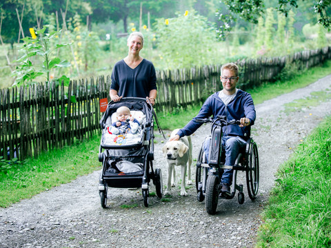 LVR-Freilichtmuseum Lindlar Eine Frau mit Kinderwagen, ein Mann im Rollstuhl mit Hund, spazieren auf einem ländlichen Weg.