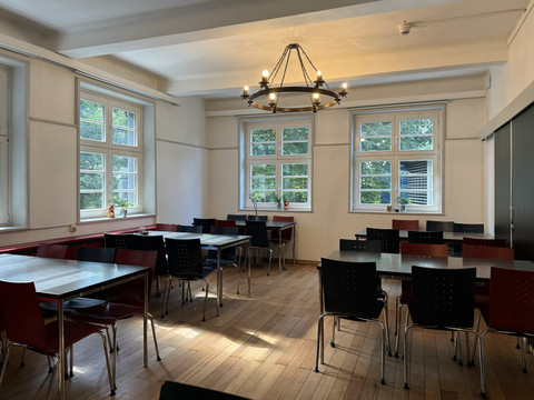 Jugendherberge Radevormwald - Speisesaal <p>Heller Raum mit Holzboden, mehreren Tischen und Stühlen, beleuchtet durch große Fenster und Kronleuchter.</p>