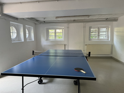 Jugendherberge Radevormwald - Ansicht Tischtennisplatte Eine Tischtennisplatte steht in einem hellen Raum mit weißen Wänden und mehreren Fenstern.