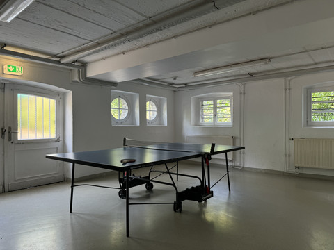 Jugendherberge Radevormwald - Ansicht Tischtennisplatte Tischtennisplatte in einem weißen, hellen Raum mit Fenstern und Heizkörper.
