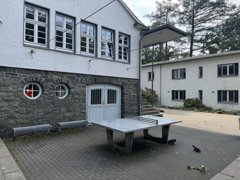 Jugendherberge Radevormwald - Außenansicht Ein Tischtennistisch auf einem gepflasterten Innenhof, umgeben von Gebäuden mit Stein- und Putzfassaden.