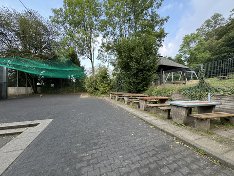 Jugendherberge Radevormwald - Ansicht Spielfläche <p>Ein gepflasterter Außenbereich mit Holzbänken und grüner Umgebung in Radevormwald.</p>