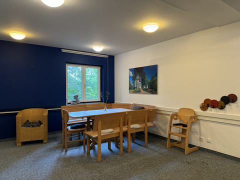 Jugendherberge Radevormwald - Aufenthaltsraum Eine gemütliche Sitzecke mit Holzmöbeln und Kinderstuhl neben einem Fenster mit Blick ins Grüne.