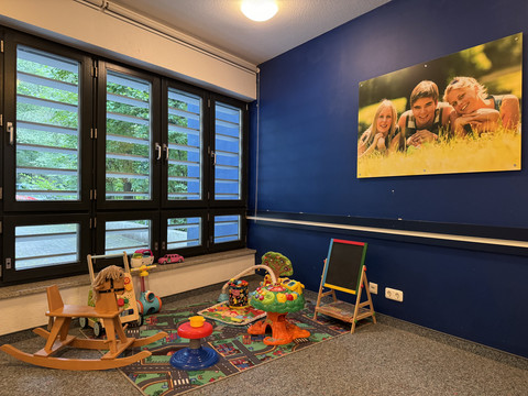 Jugendherberge Radevormwald - Ansicht Aufenthaltsraum Eine bunte Spielecke mit Spielzeug, Schaukelpferd und Bild von lachenden Kindern an der Wand.
