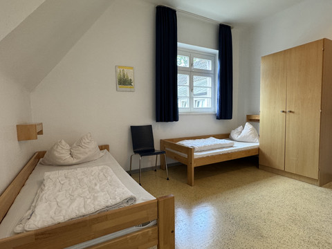 Jugendherberge Radevormwald - Ansicht Doppelzimmer Zwei Einzelbetten in hellem, schlichtem Zimmer mit Schrank und Fenster, blau-graue Akzente.