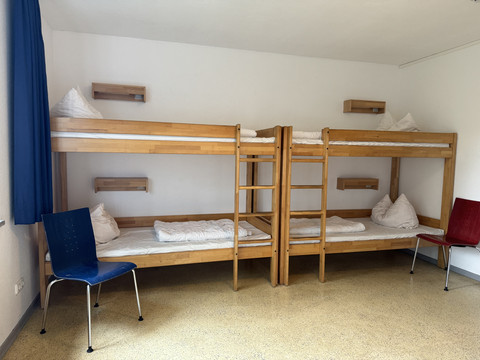 Jugendherberge Radevormwald - Ansicht Viererzimmer Vier Holz-Etagenbetten, einladend und ordentlich, mit blauen und roten Stühlen im Raum verteilt.