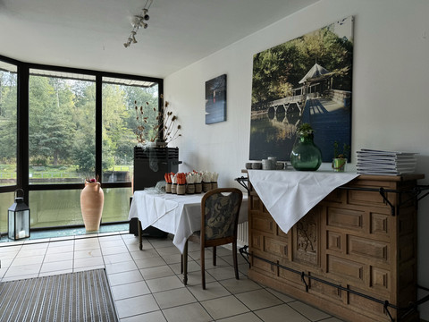 Café-Restaurant Uelfetal - Ansicht Eingangsbereich Einladender Wintergarten mit großen Fenstern, Blick auf Wald und See, dekoriert mit Blumenarrangements.