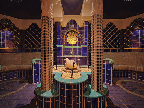 Luxuriöses Spa mit blauen und grünen Kacheln, zentralem Brunnen und kunstvollen Säulen, schafft eine entspannende Atmosphäre.