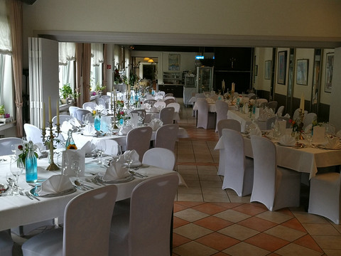 Uelfetal_2.jpg Ein eleganter Speisesaal mit weiß gedeckten Tischen, dekorativen Blumen und sanftem natürlichem Licht.