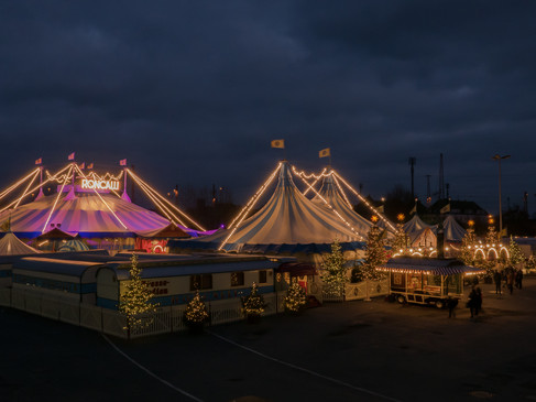 Ein beleuchtetes Zirkuszelt bei Nacht mit festlichen Lichtern und einer stimmungsvollen Atmosphäre.