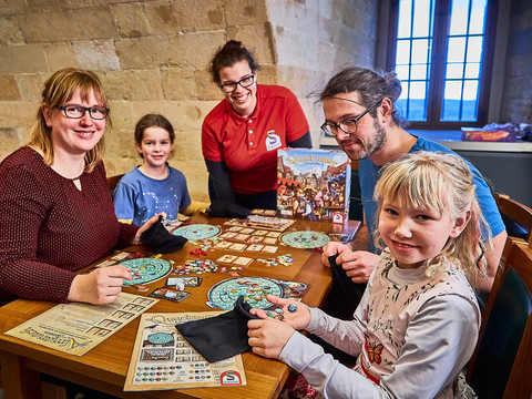 Mensen van verschillende leeftijden spelen samen bordspellen in een gezellige ruimte met stenen muren.
