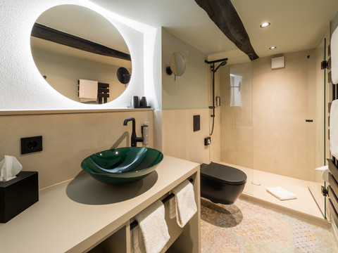 Hotel von Landsberg Modernes Badezimmer mit rundem Spiegel, grünem Waschbecken und offener Regendusche. Dezente Beleuchtung.