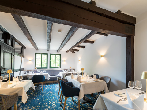 Hotel von Landsberg Ein elegantes Restaurant mit Holzbalken, weißen Tischdecken und einem blauen Teppich; stilvoll gedeckt.