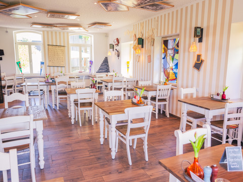 Café Die alte Schule Ein gemütliches, hell eingerichtetes Café mit Holzboden und ansprechend dekorierten Wänden und Decke.