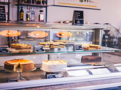 Café Die alte Schule Auswahl an hausgemachten Kuchen hinter Glasvitrine in einem Café, darunter Käse- und Schokoladenkuchen.