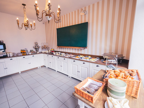 Café Die alte Schule Gemütlicher Frühstücksraum mit Buffet, warmen Tönen, Kronleuchtern und gedeckter Tafel im Landhausstil.